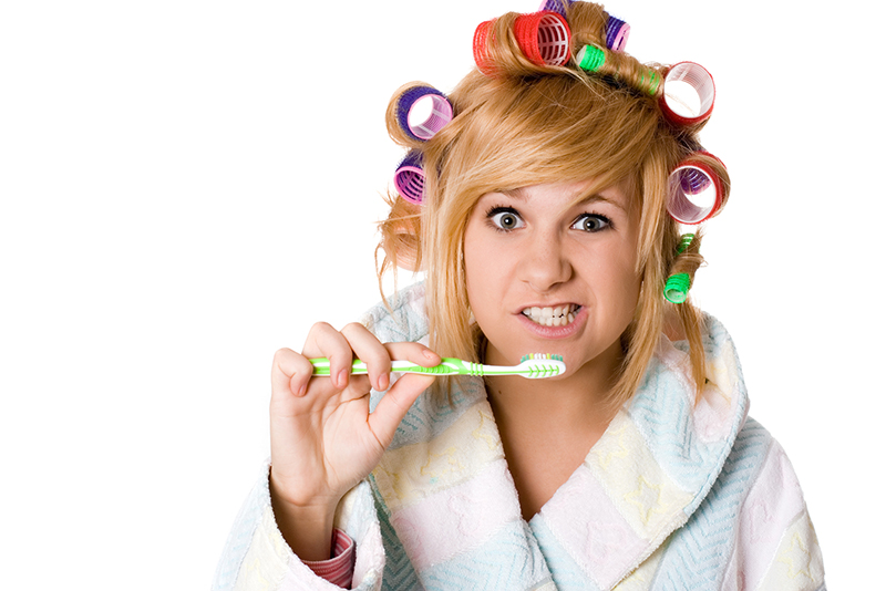 woman in bathrobe and hair rollers and brushing teeth
